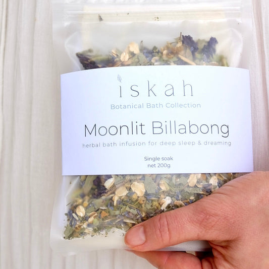 A hand holding a packet of herbs and magnesium bath salts.