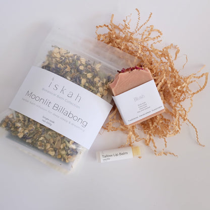 Packaged products  of a soap, herbal bath and lip balm with visible branding on a light background