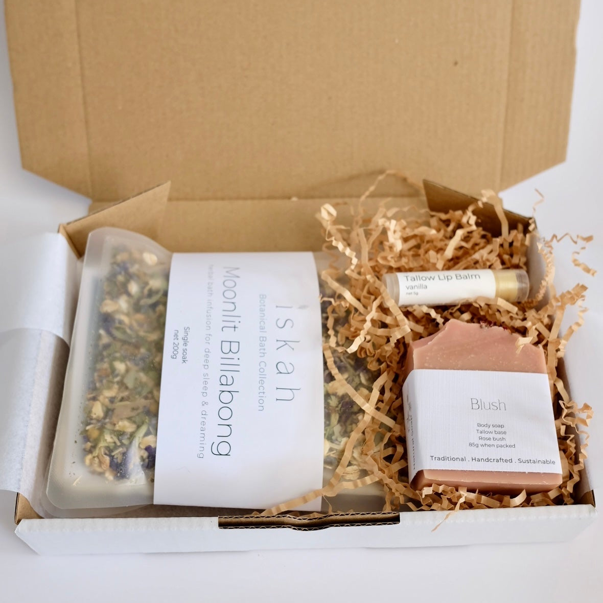 Open cardboard box with natural products including a soap bar and a jar on a white background